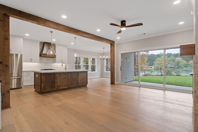 kitchen with a kitchen island with sink, hanging light fixtures, wall chimney exhaust hood, stainless steel fridge, and a healthy amount of sunlight