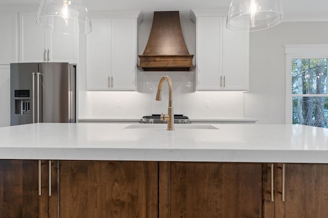 kitchen featuring white cabinets, an island with sink, hanging light fixtures, and custom exhaust hood