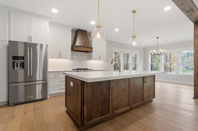 kitchen with hanging light fixtures, stainless steel fridge with ice dispenser, an island with sink, light hardwood / wood-style floors, and custom range hood