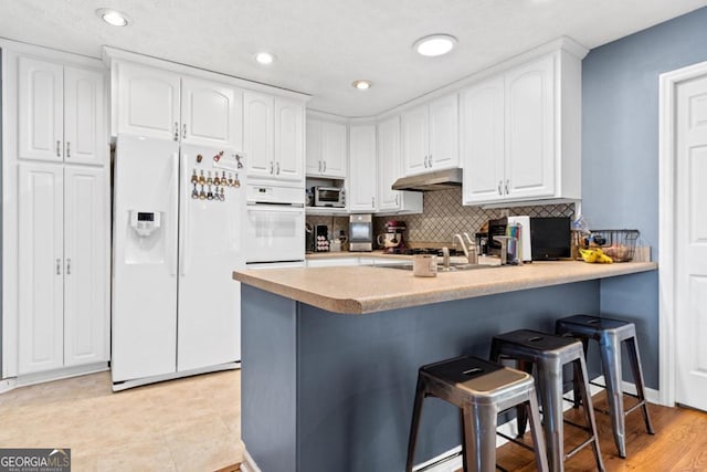 kitchen featuring a peninsula, white appliances, tasteful backsplash, a kitchen breakfast bar, and white cabinetry