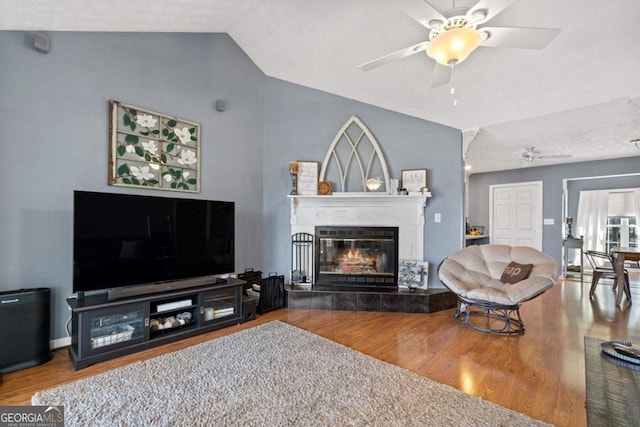 living area featuring lofted ceiling, a ceiling fan, a tiled fireplace, and wood finished floors