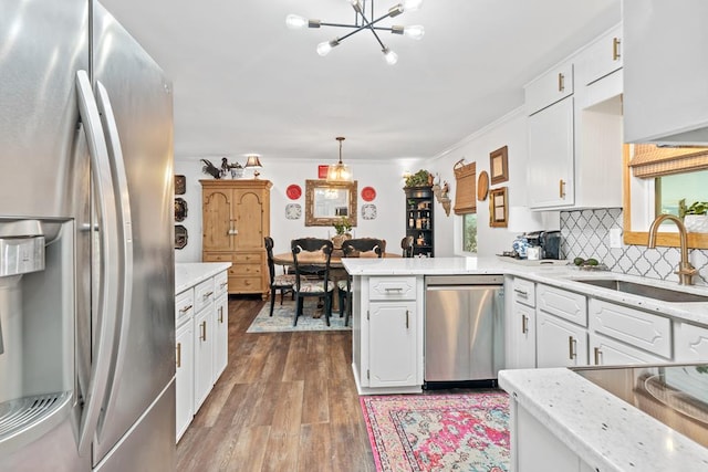 kitchen with white cabinetry, sink, hanging light fixtures, stainless steel appliances, and kitchen peninsula