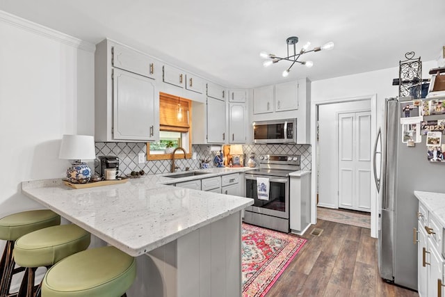 kitchen with sink, dark hardwood / wood-style flooring, kitchen peninsula, a kitchen bar, and appliances with stainless steel finishes