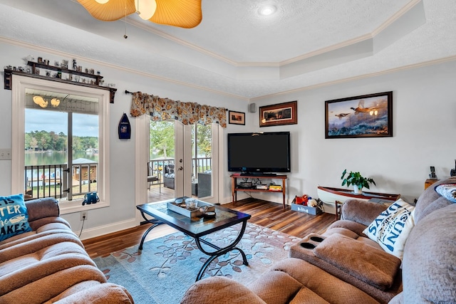 living room with a water view, crown molding, ceiling fan, a tray ceiling, and wood-type flooring