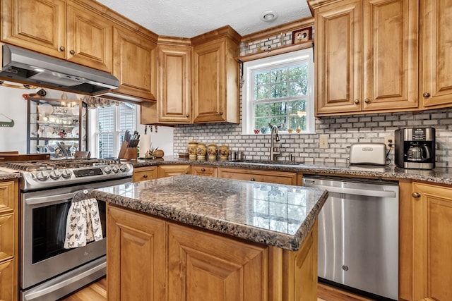 kitchen with sink, decorative backsplash, dark stone countertops, appliances with stainless steel finishes, and a kitchen island