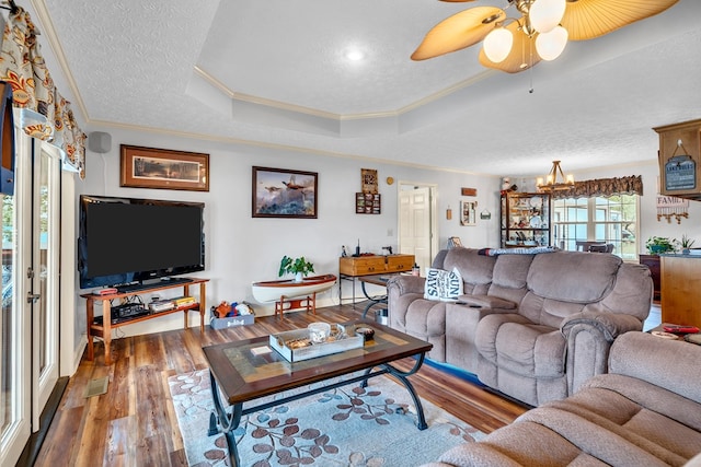 living room with crown molding, hardwood / wood-style floors, a textured ceiling, a tray ceiling, and ceiling fan with notable chandelier