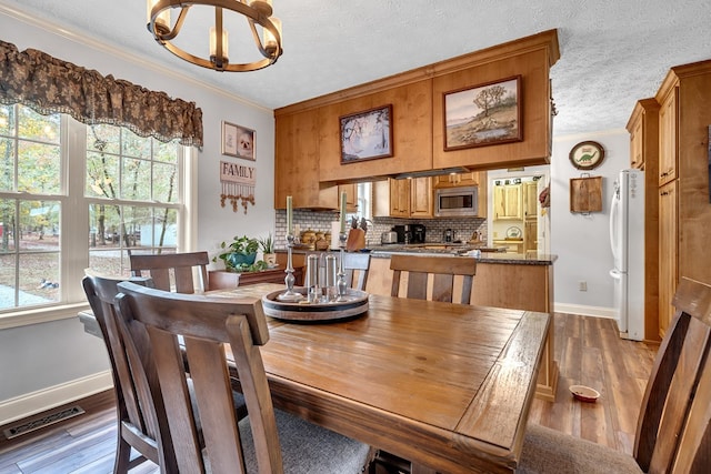 dining room with hardwood / wood-style floors, a chandelier, a textured ceiling, and ornamental molding