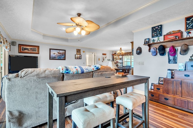 dining area with a raised ceiling, light hardwood / wood-style flooring, a textured ceiling, ceiling fan with notable chandelier, and ornamental molding