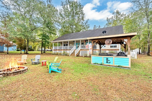 rear view of property featuring a porch, a yard, and a fire pit