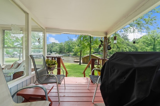 wooden terrace with a grill, a lawn, a water view, and view of wooded area