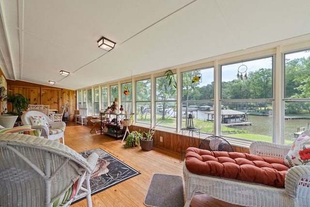 sunroom / solarium with lofted ceiling, a water view, wood-type flooring, and wooden walls