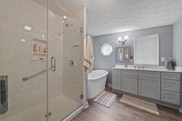 full bathroom with a stall shower, a textured ceiling, wood finished floors, vanity, and a soaking tub