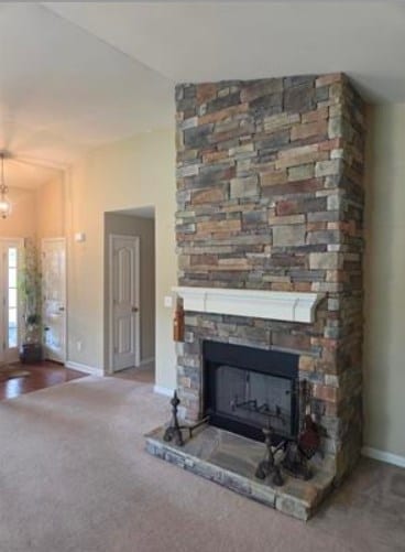 179 Garrett Dr, Eatonton, GA 31024 - unfurnished living room featuring a stone fireplace, carpet floors, and a chandelier