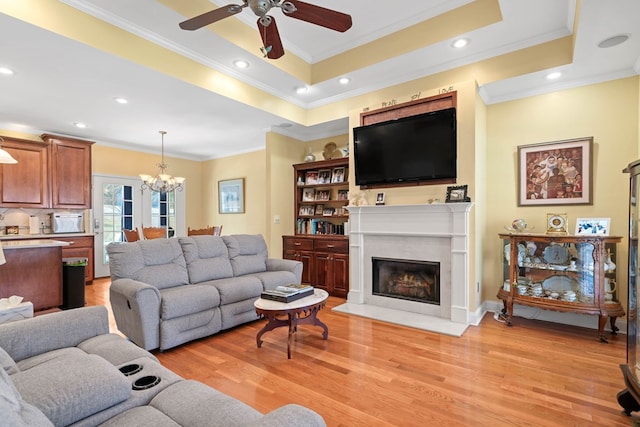 living area with light wood-style flooring, a raised ceiling, crown molding, and ceiling fan with notable chandelier