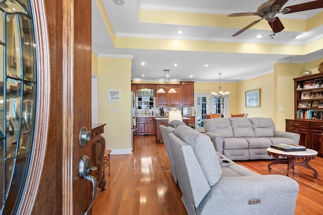 living area with light wood-style flooring, a tray ceiling, and ornamental molding