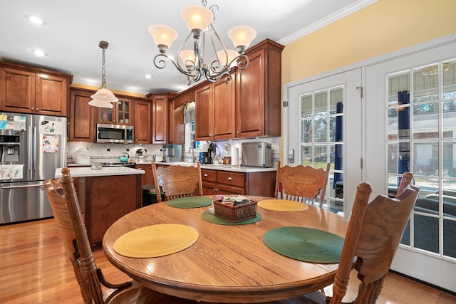 dining room with light wood-type flooring, a healthy amount of sunlight, ornamental molding, and an inviting chandelier