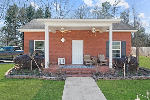 exterior space with roof with shingles, brick siding, a lawn, fence, and ceiling fan