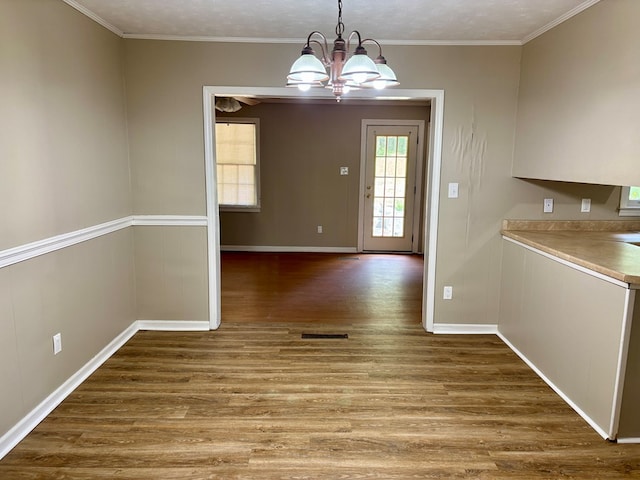 unfurnished dining area featuring an inviting chandelier, visible vents, baseboards, ornamental molding, and wood finished floors