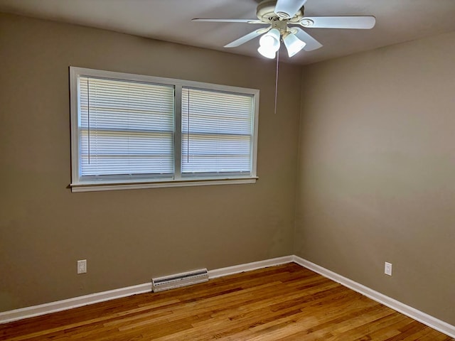empty room featuring a wealth of natural light, a ceiling fan, visible vents, baseboards, and wood finished floors