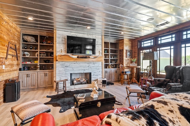 living room with built in shelves, a fireplace, wooden walls, and light hardwood / wood-style flooring