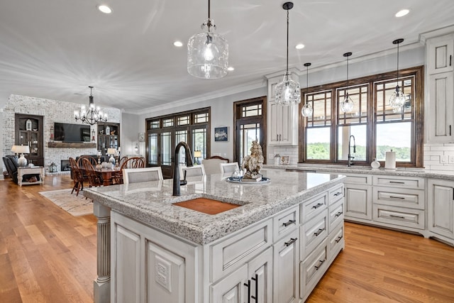 kitchen featuring a center island with sink, sink, hanging light fixtures, and light hardwood / wood-style flooring