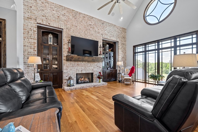 living room featuring ceiling fan, high vaulted ceiling, hardwood / wood-style flooring, and a brick fireplace