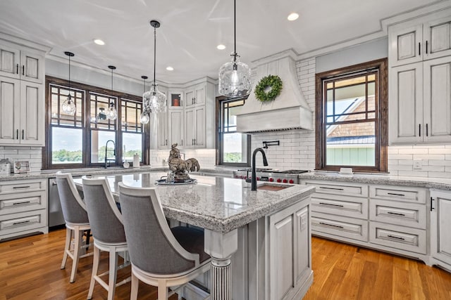 kitchen featuring light stone countertops, tasteful backsplash, an island with sink, a kitchen bar, and custom exhaust hood