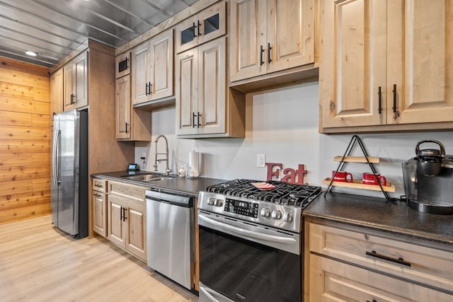 kitchen with appliances with stainless steel finishes, light hardwood / wood-style floors, wooden walls, and sink