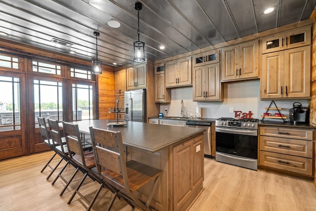 kitchen with appliances with stainless steel finishes, light wood-type flooring, sink, pendant lighting, and a kitchen island