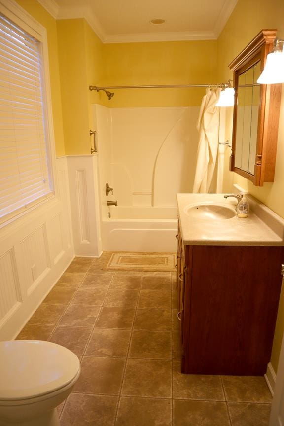 full bathroom featuring toilet, a wainscoted wall, ornamental molding, vanity, and shower / bathing tub combination