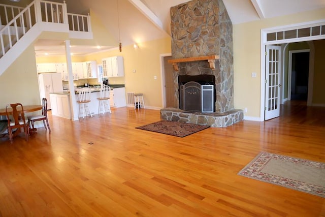 unfurnished living room featuring high vaulted ceiling, a fireplace, wood finished floors, stairway, and beam ceiling