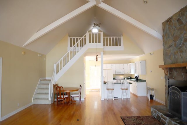 living room with stairway, a stone fireplace, high vaulted ceiling, light wood-type flooring, and beamed ceiling