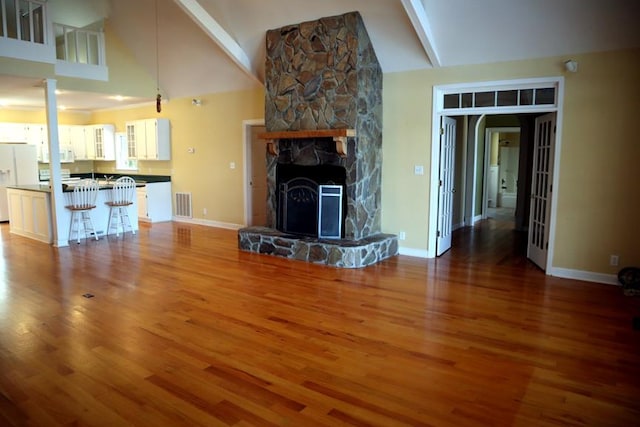 unfurnished living room featuring baseboards, visible vents, wood finished floors, a fireplace, and beam ceiling