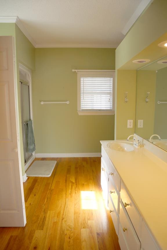 full bathroom with a stall shower, baseboards, ornamental molding, wood finished floors, and vanity