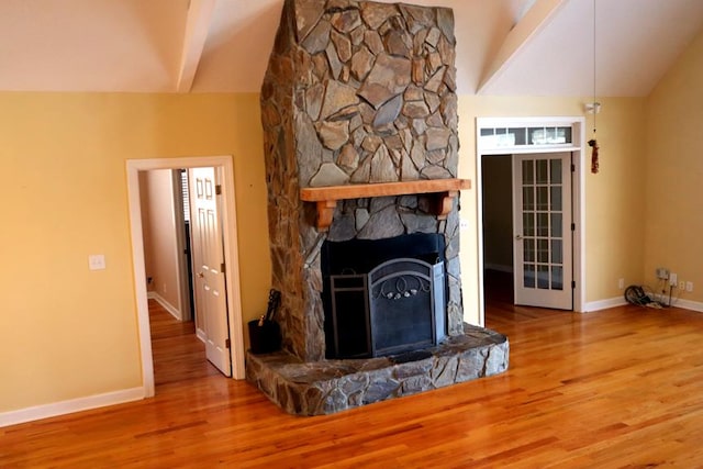 unfurnished living room featuring lofted ceiling with beams, baseboards, wood finished floors, and a stone fireplace