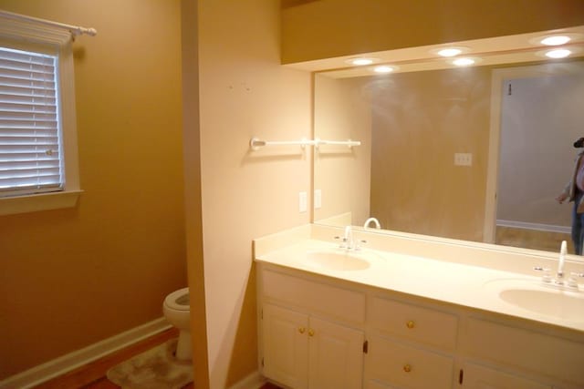 full bath featuring toilet, a sink, baseboards, and double vanity