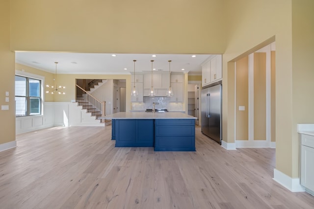 kitchen with blue cabinets, pendant lighting, a kitchen island with sink, stainless steel built in fridge, and white cabinets