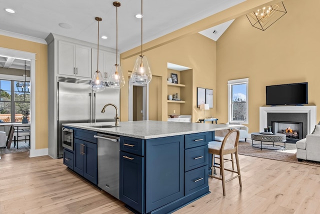 kitchen featuring sink, hanging light fixtures, stainless steel dishwasher, blue cabinetry, and a center island with sink