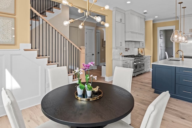 dining space with ornamental molding, sink, a chandelier, and light hardwood / wood-style flooring