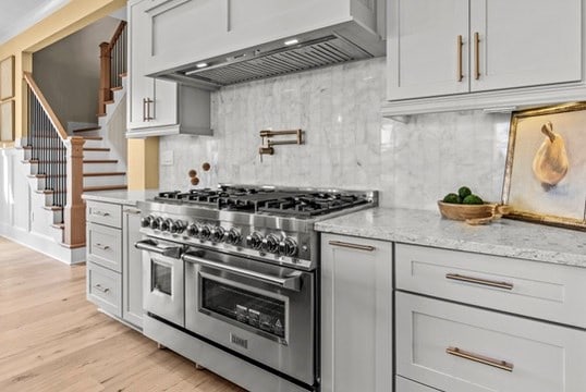 kitchen with light hardwood / wood-style flooring, light stone counters, tasteful backsplash, custom exhaust hood, and range with two ovens