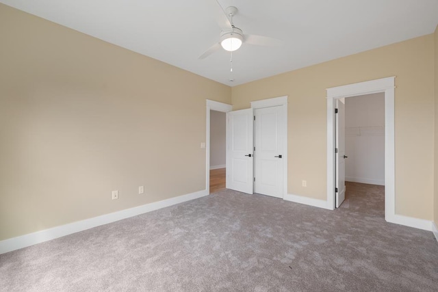 unfurnished bedroom featuring ceiling fan, a walk in closet, a closet, and carpet