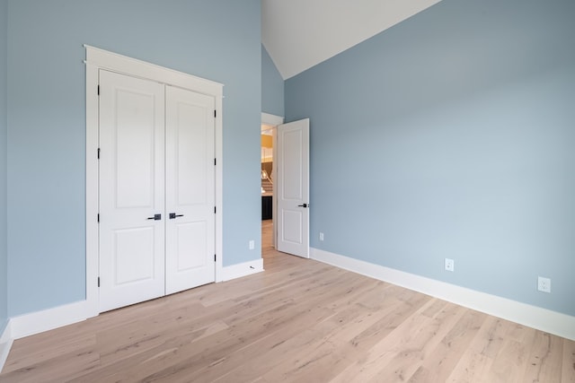 unfurnished bedroom with a closet, high vaulted ceiling, and light wood-type flooring