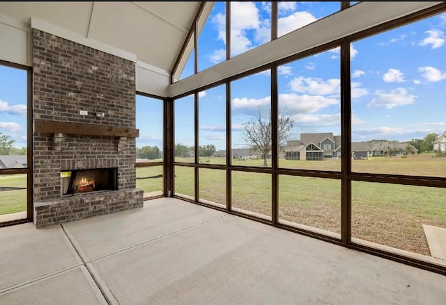 unfurnished sunroom featuring vaulted ceiling, a brick fireplace, and a healthy amount of sunlight