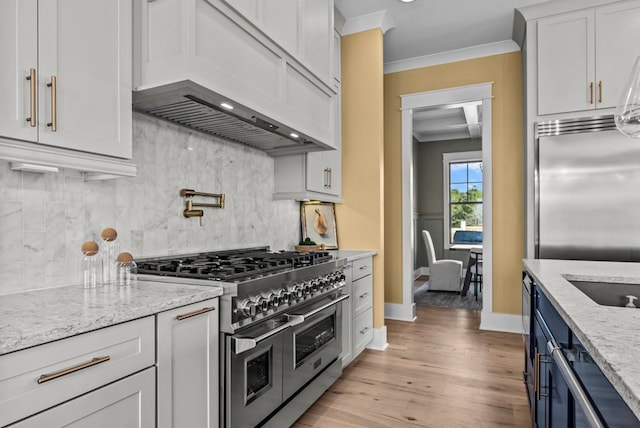 kitchen featuring high quality appliances, custom range hood, white cabinets, light stone countertops, and backsplash