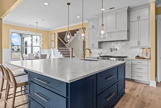 kitchen with sink, a kitchen bar, hanging light fixtures, blue cabinetry, and a center island with sink