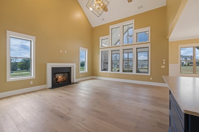 unfurnished living room with light wood-type flooring, an inviting chandelier, and high vaulted ceiling