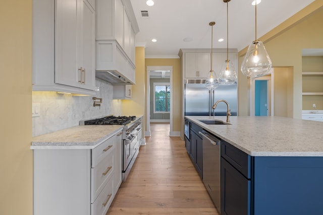 kitchen with high end appliances, sink, decorative light fixtures, white cabinets, and light hardwood / wood-style floors