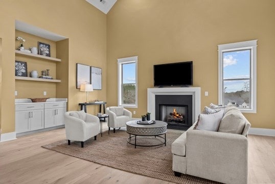 living area with high vaulted ceiling, light hardwood / wood-style flooring, and built in features