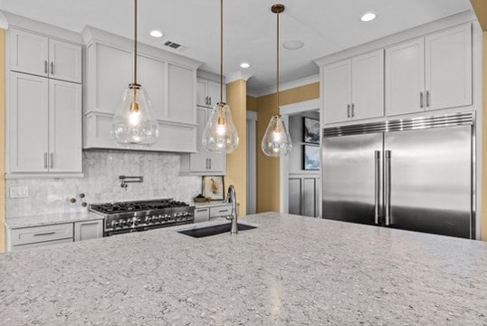 kitchen featuring high end appliances, sink, hanging light fixtures, and white cabinets