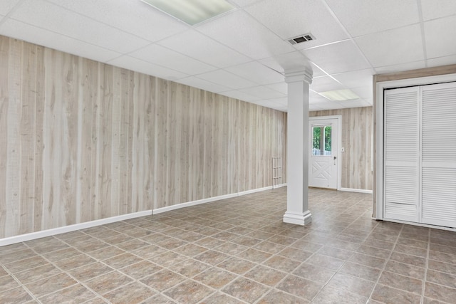 below grade area featuring wood walls, baseboards, visible vents, and a drop ceiling
